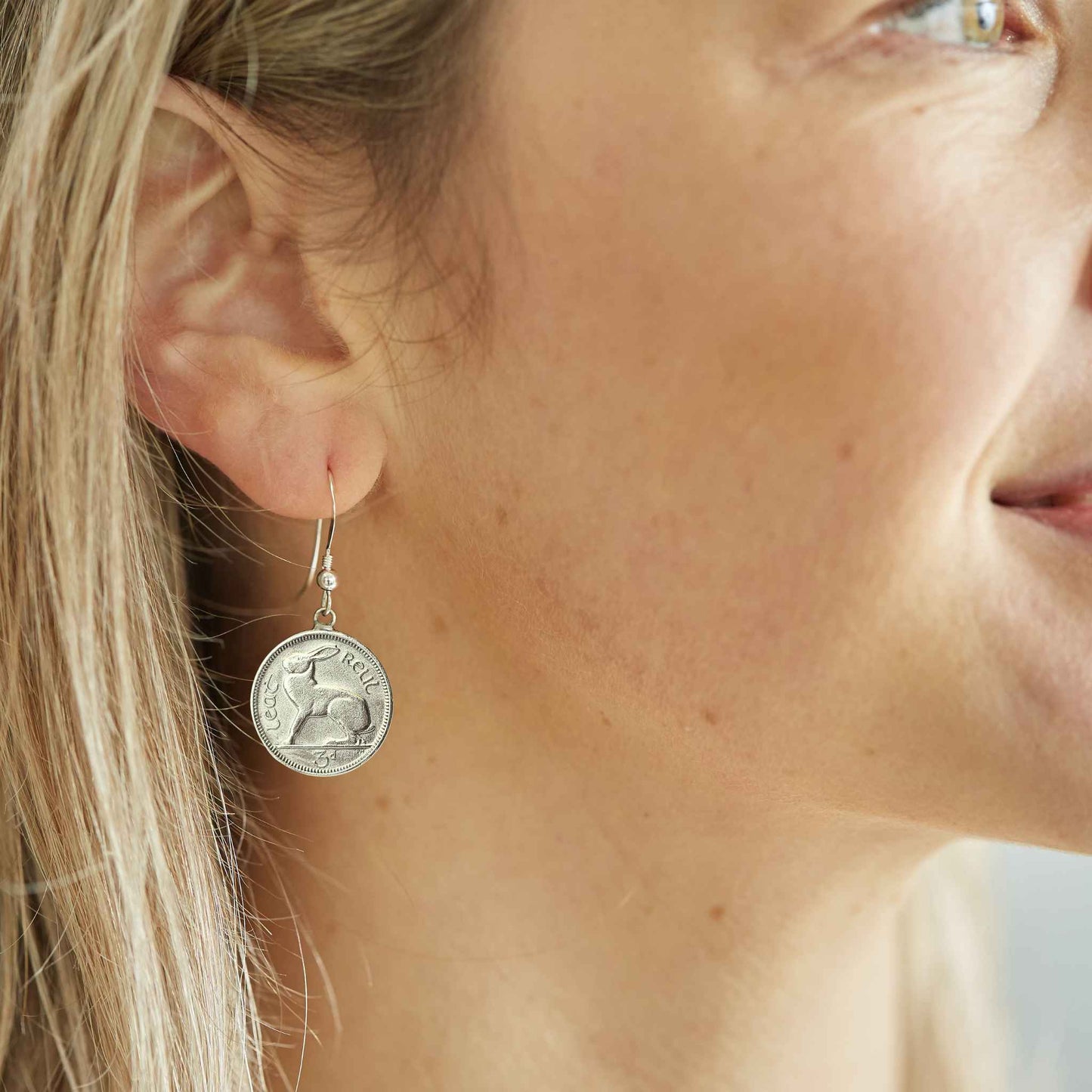 Close-up of a woman wearing a silver Irish threepence coin earring with sterling silver ear wire.