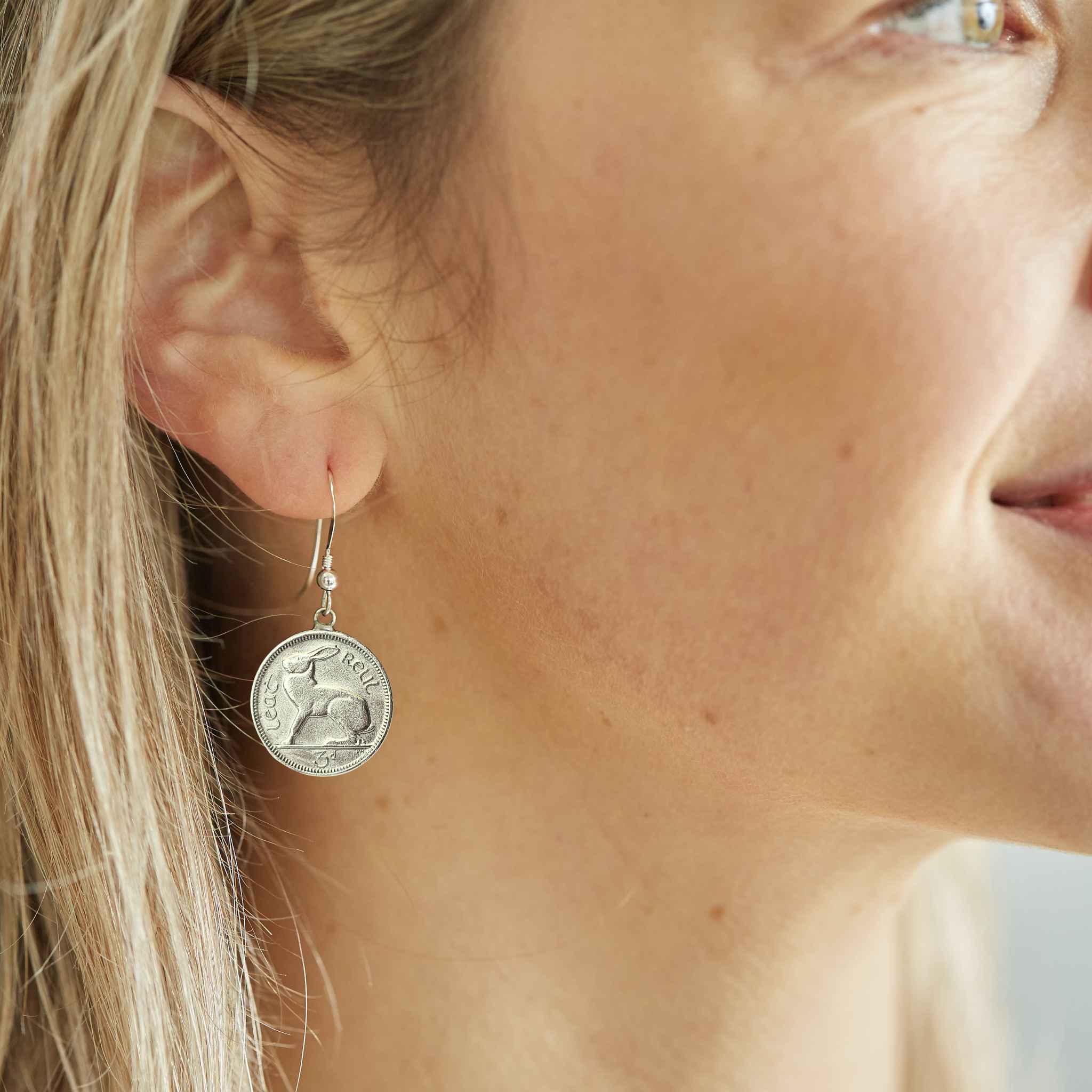 Close-up of a woman wearing a silver Irish threepence coin earring with sterling silver ear wire.