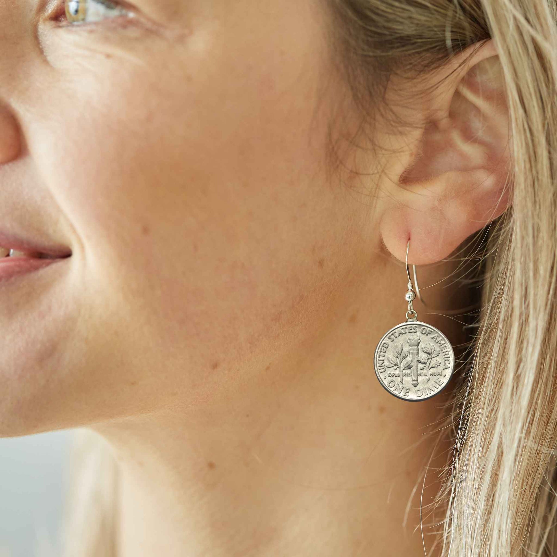 Close-up of a woman wearing a silver American Dime coin earring suspended on sterling silver ear wire.