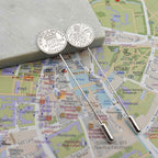 Two silver tie pins with British Sixpence coins with a map of Cambridge city in the background