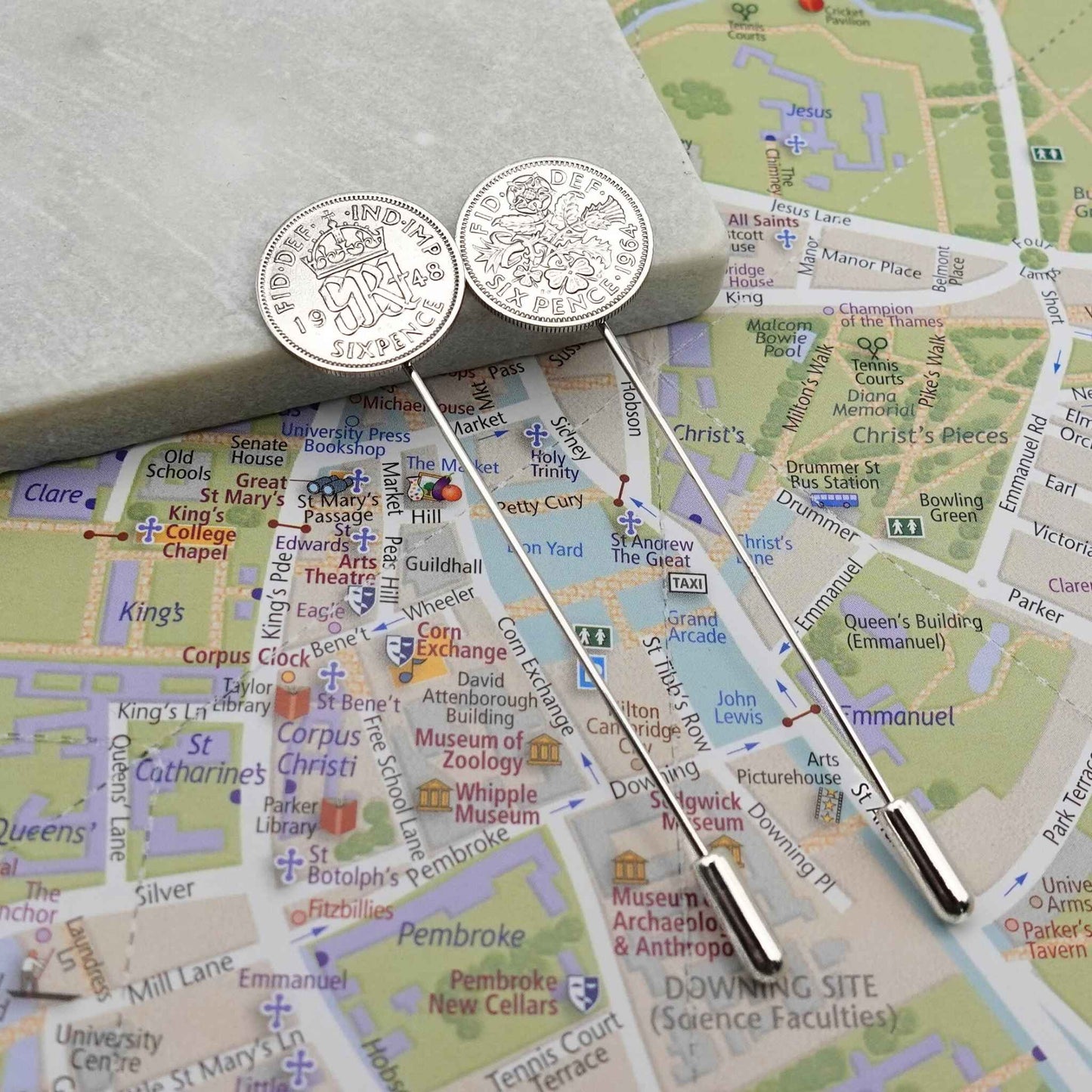 Two silver tie pins with British Sixpence coins with a map of Cambridge city in the background