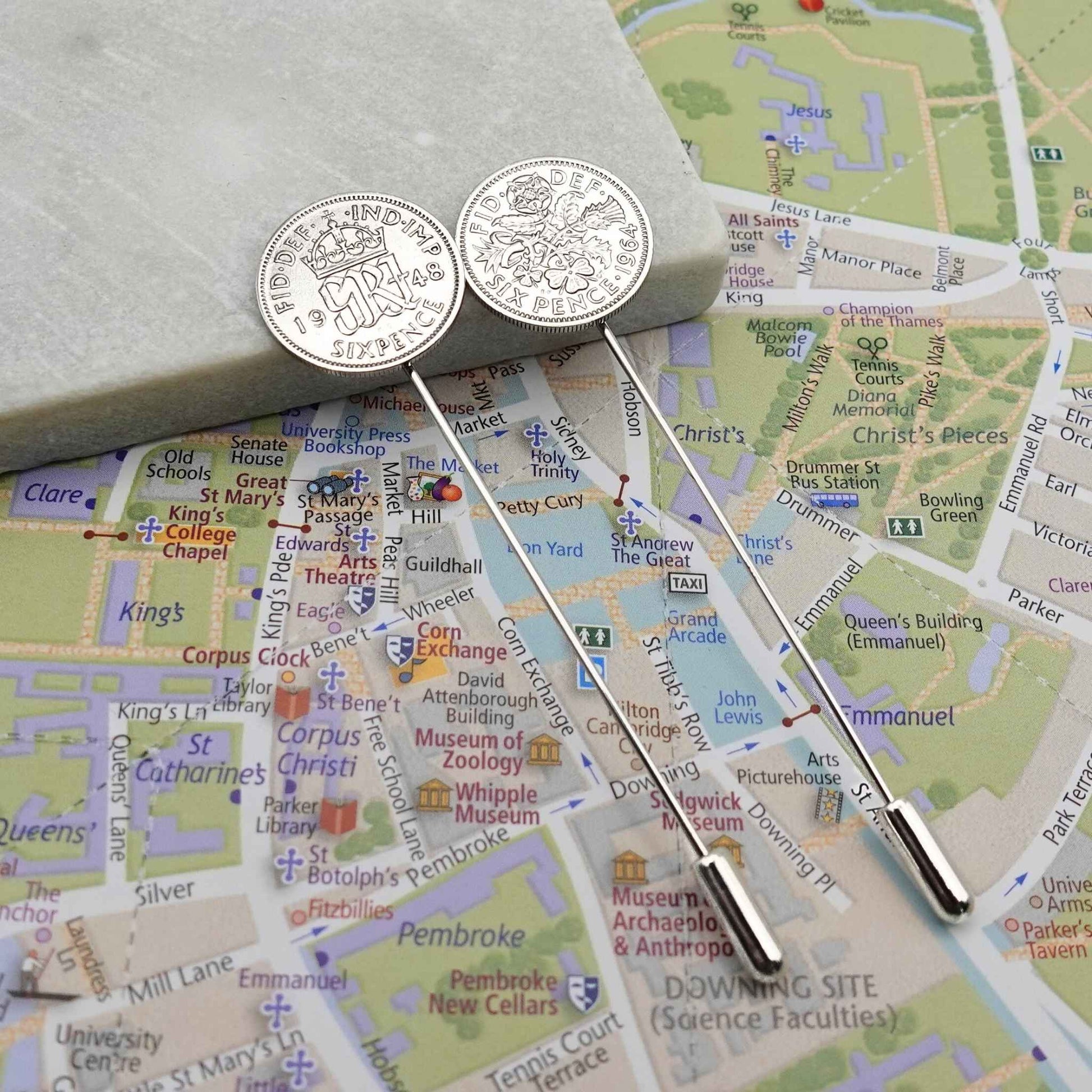 Two silver tie pins with British Sixpence coins with a map of Cambridge city in the background