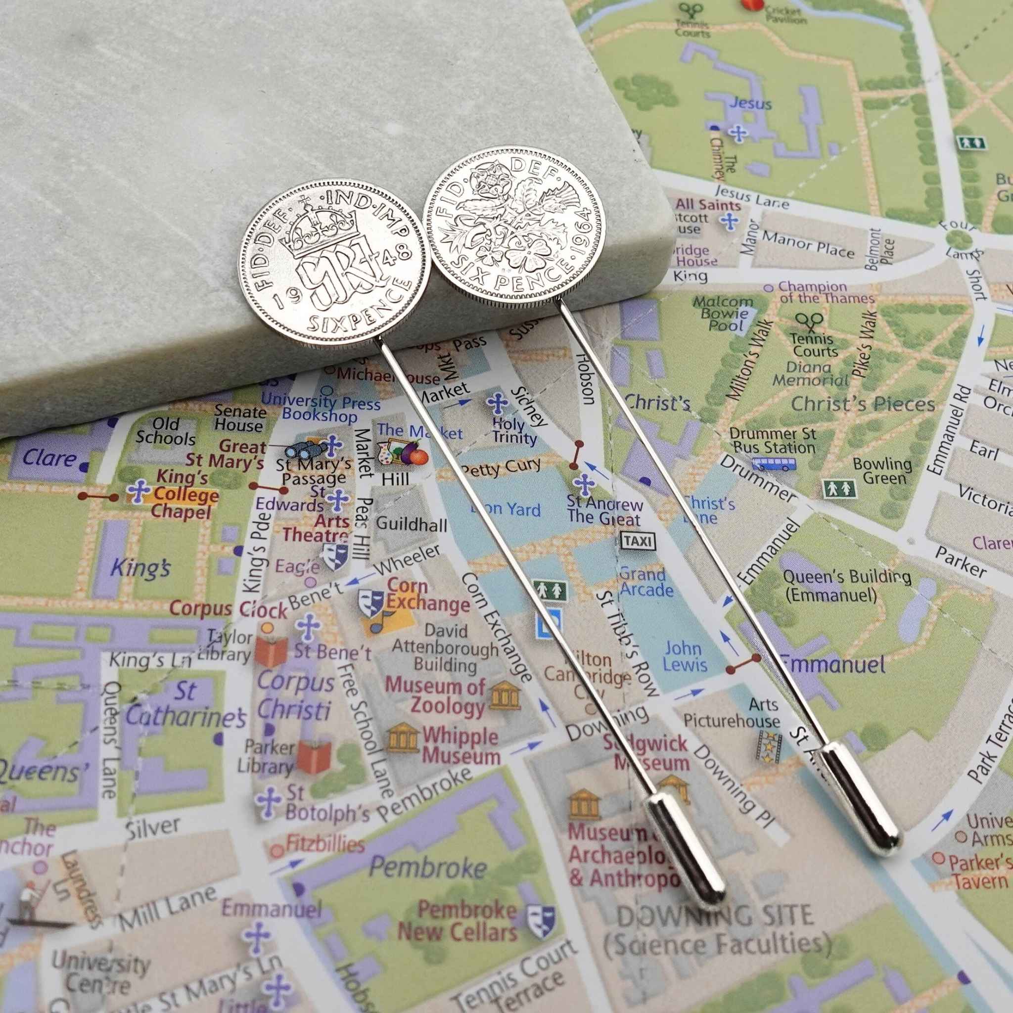 Two silver tie pins with British Sixpence coins with a map of Cambridge city in the background
