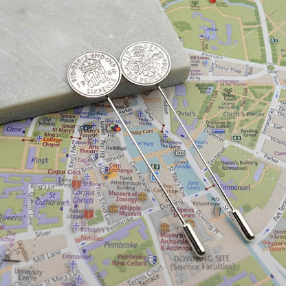 Two silver tie pins with British Sixpence coins with a map of Cambridge city in the background