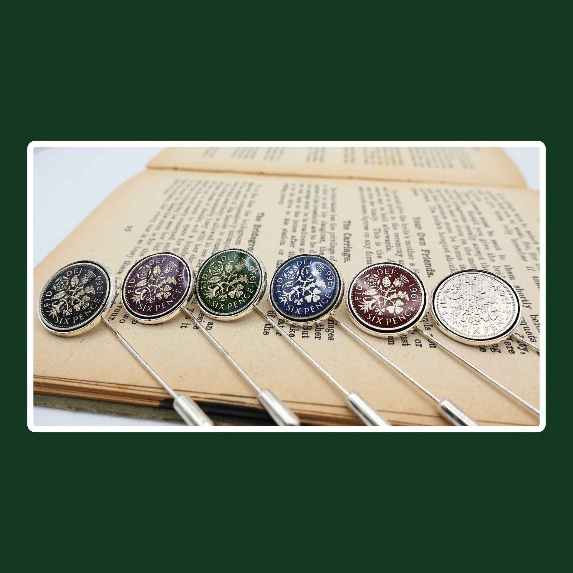 Set of six hand enamelled coloured British Queen Elizabeth 2nd sixpence coin silver plated tie pins with stoppers on book.