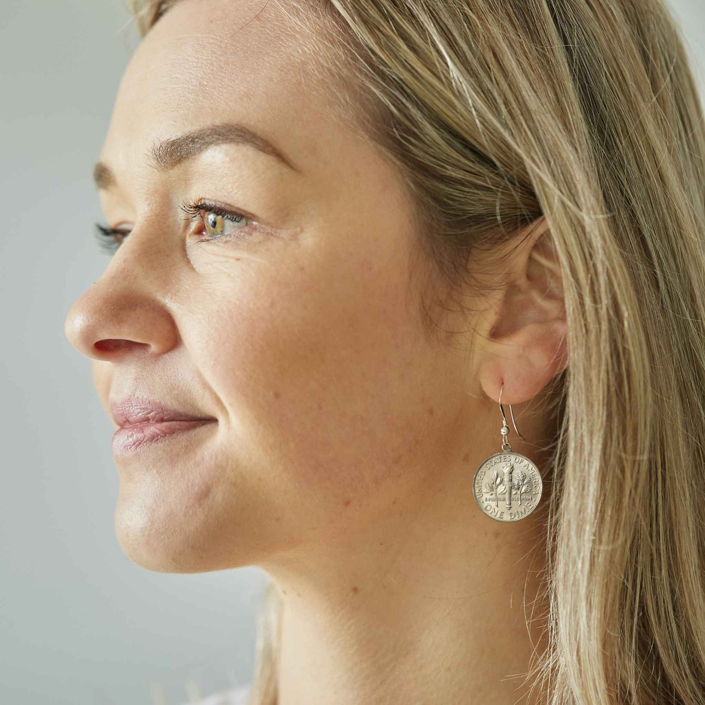 Close-up of a woman wearing an American Dime silver coin earring against a neutral background