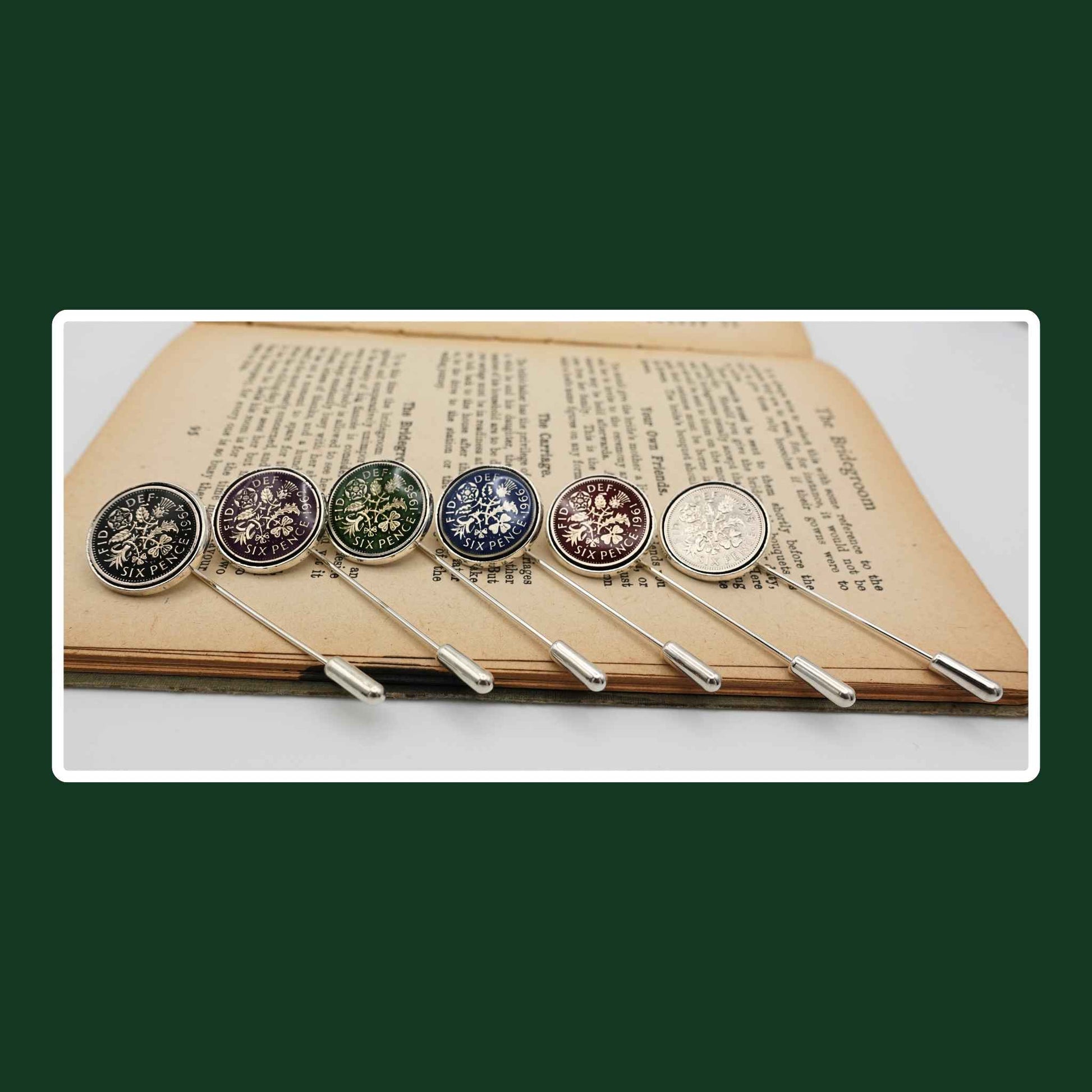 Set of six hand enamelled coloured British Queen Elizabeth 2nd sixpence coin silver plated tie pins on book.
