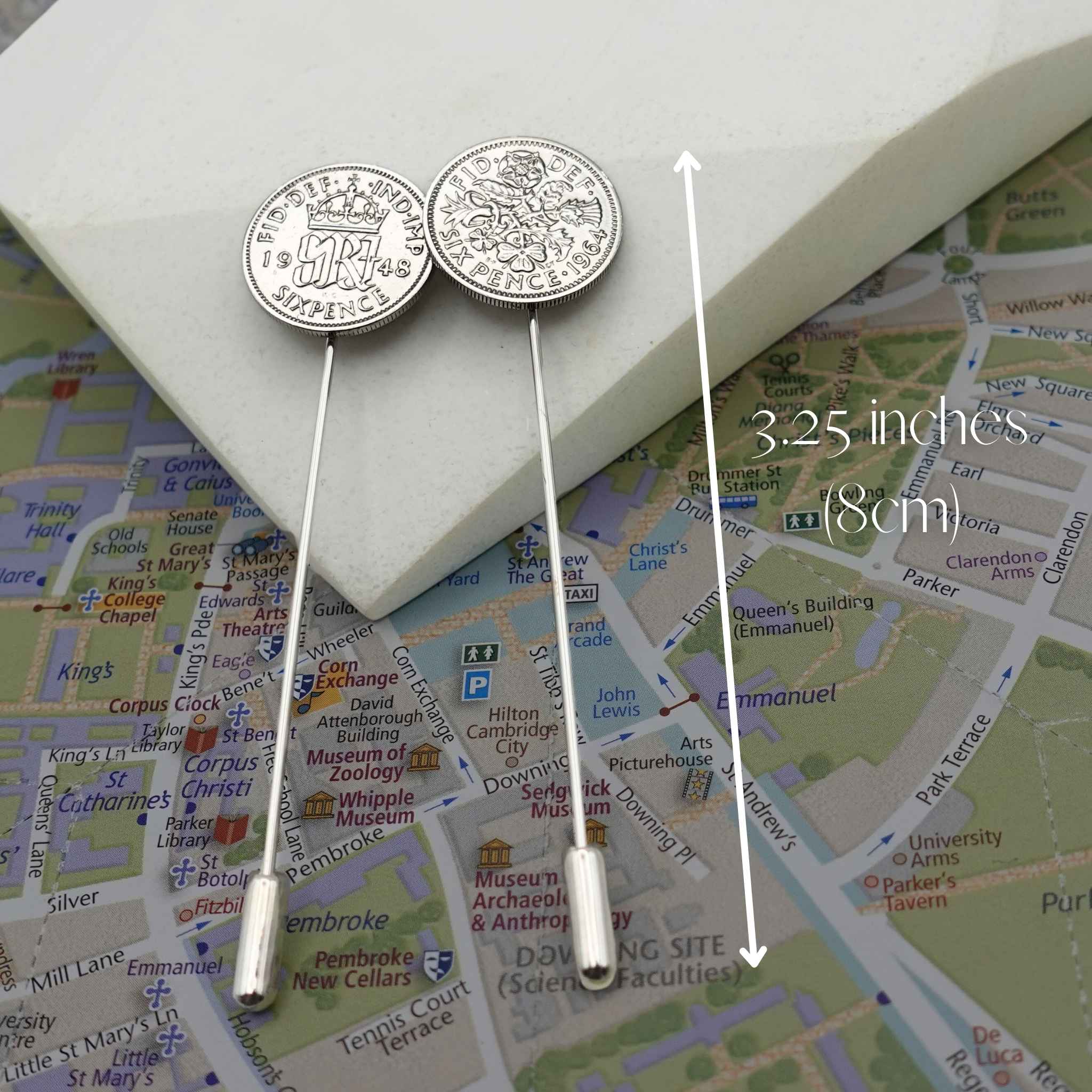 Two silver sixpence coin tie pins on a Cambridge map with measurement label