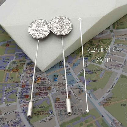 Two silver sixpence coin tie pins on a Cambridge map with measurement label
