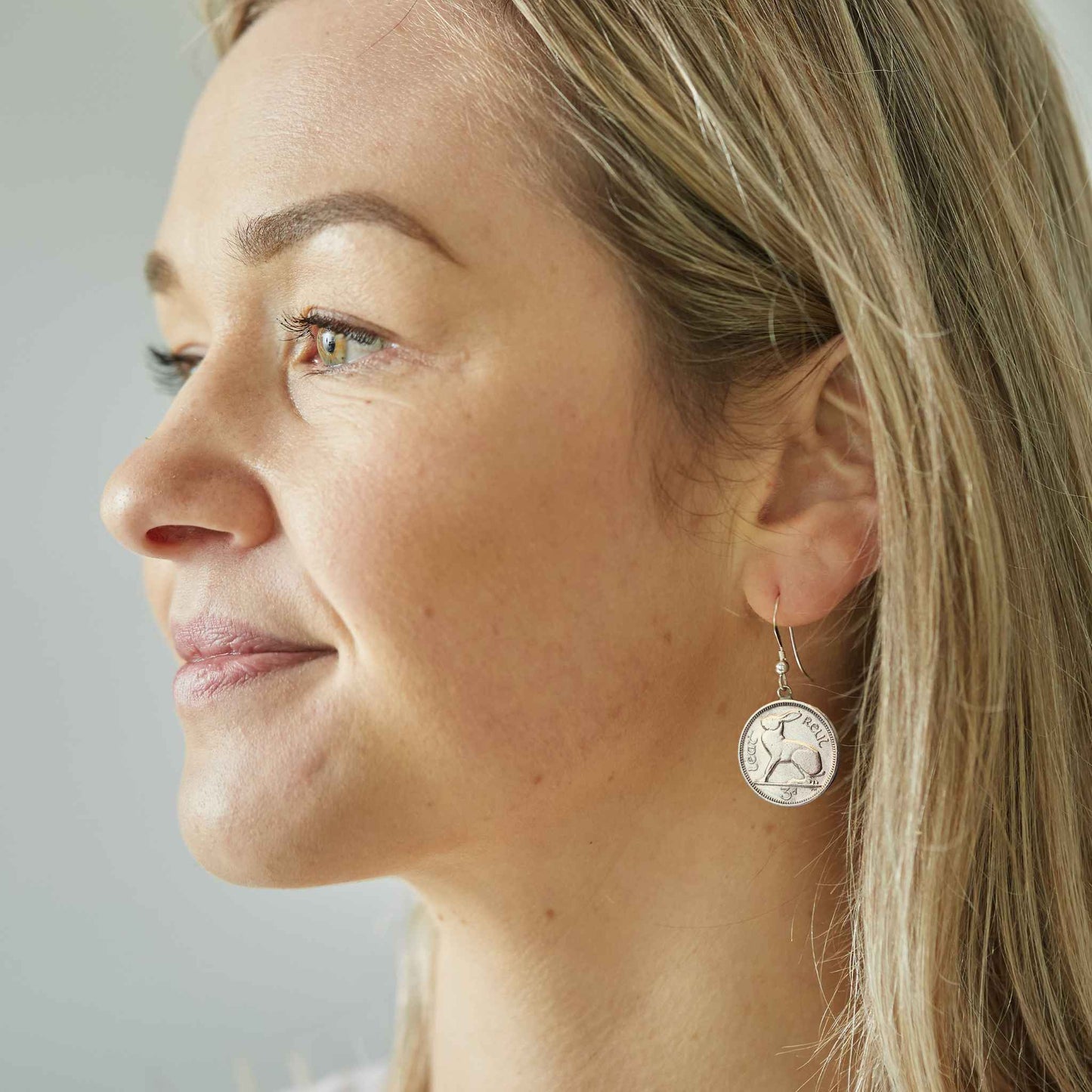 Close-up of a woman wearing a silver Irish threepence coin earring featuring a hare or rabbit animal with sterling silver ear wire.
