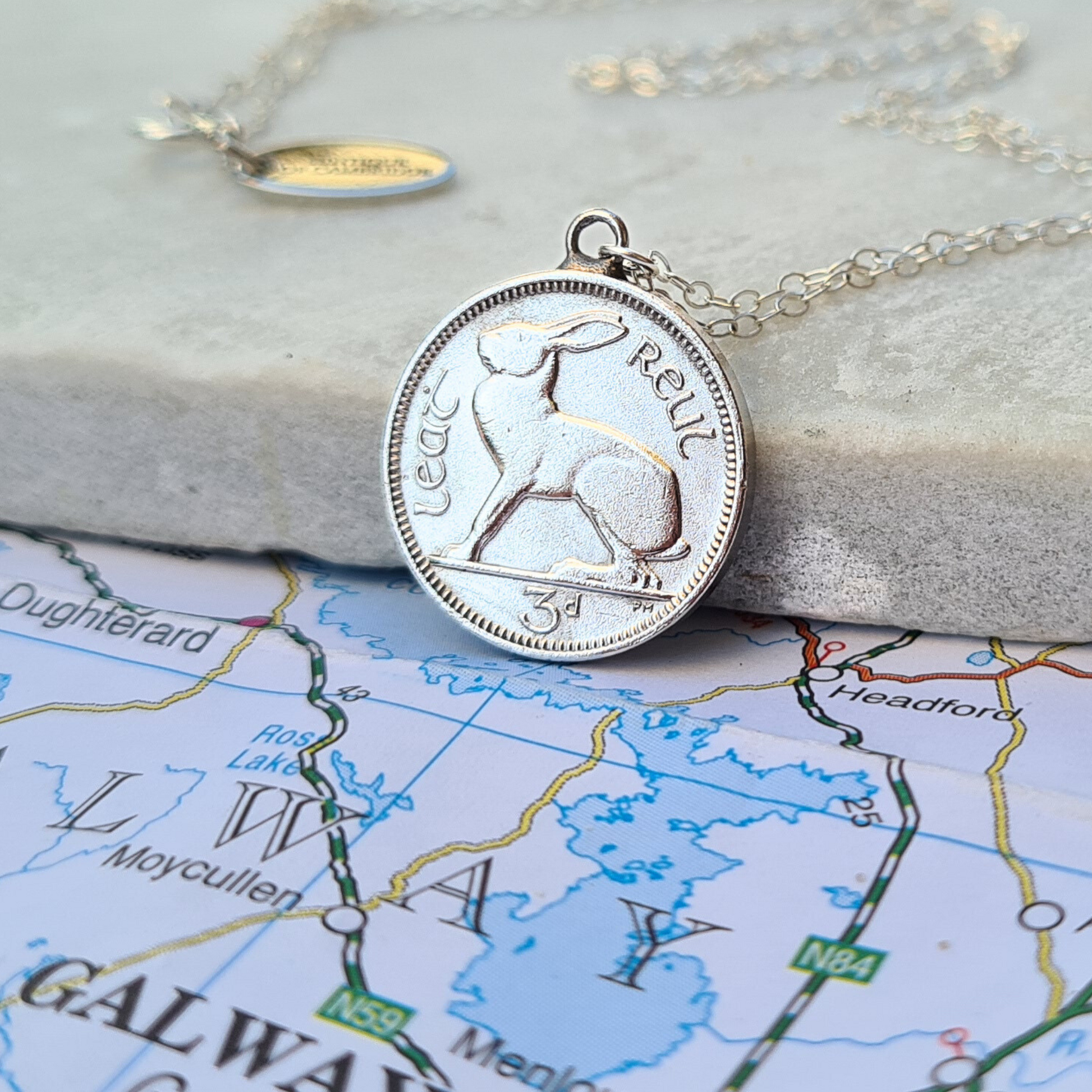 Silver coin Irish threepence (hare) coin pendant on a necklace lying on a map