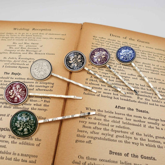 Set of decorative British sixpence coin enamelled hair slides on an open book