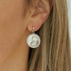 Close-up of a person wearing an Irish threepence silver coin earring with a rabbit design.