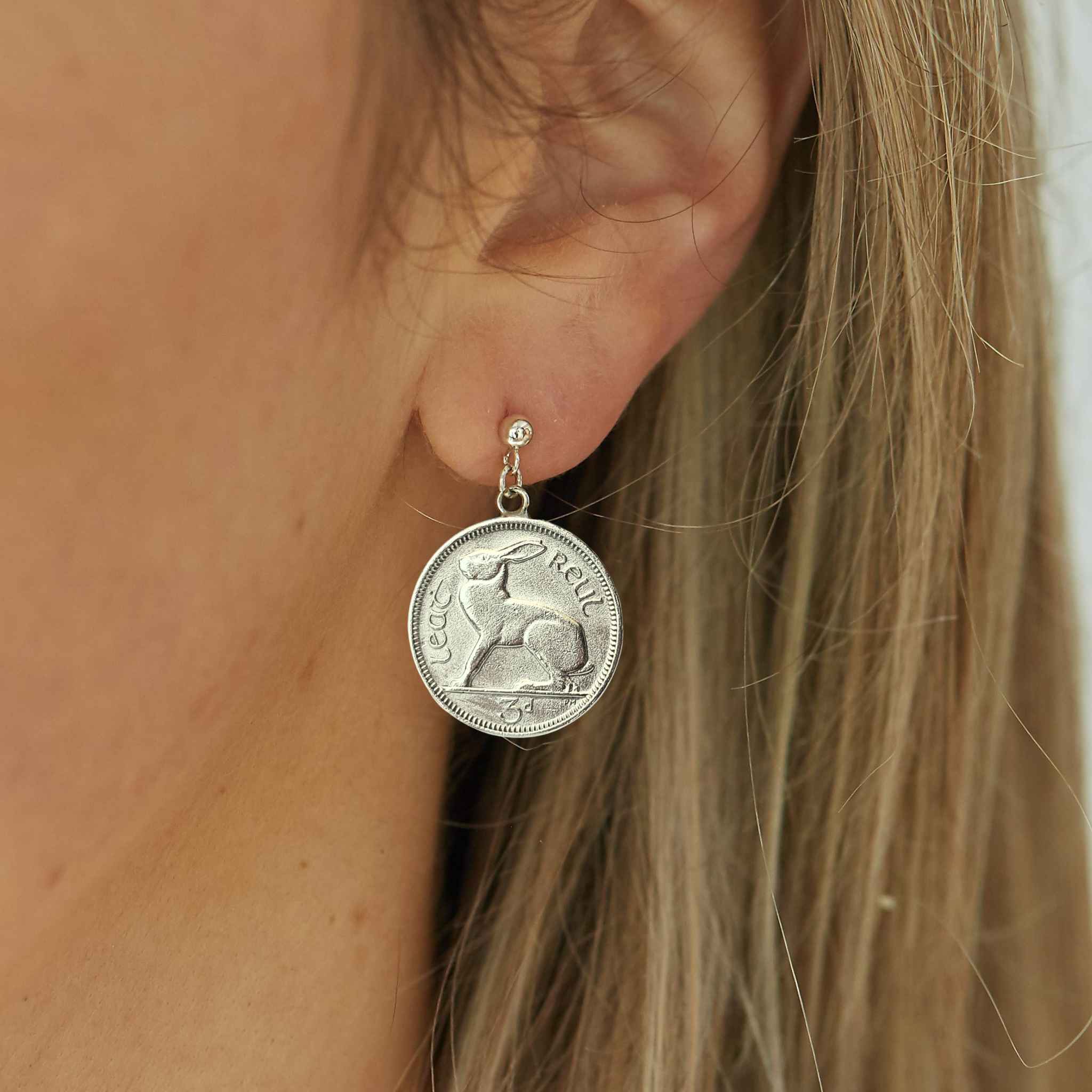 Close-up of a person wearing an Irish threepence silver coin earring with a rabbit design.