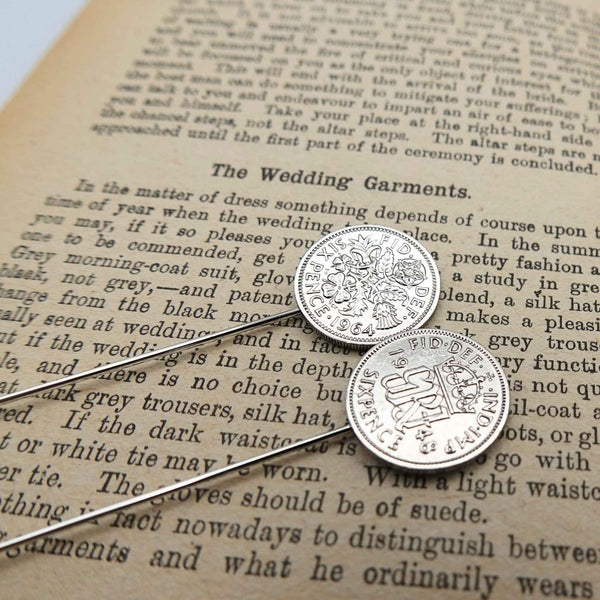 Two silver british sixpence coin tie pins with a coat of arms on an old book page.