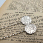 Two silver british sixpence coin tie pins with a coat of arms on an old book page.