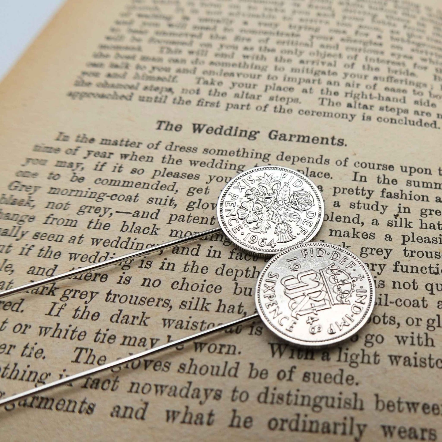 Two silver british sixpence coin tie pins with a coat of arms on an old book page.