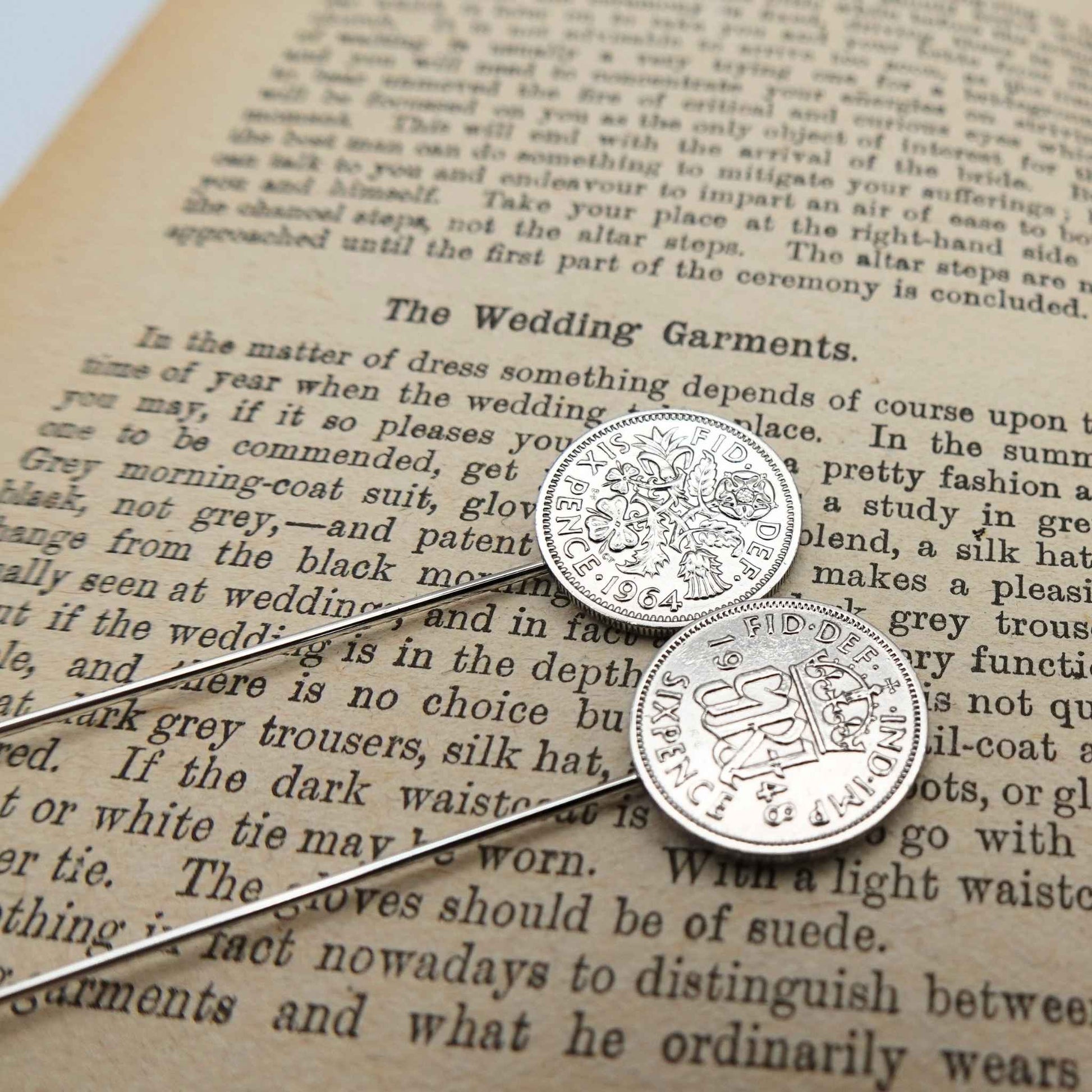 Two silver british sixpence coin tie pins with a coat of arms on an old book page.