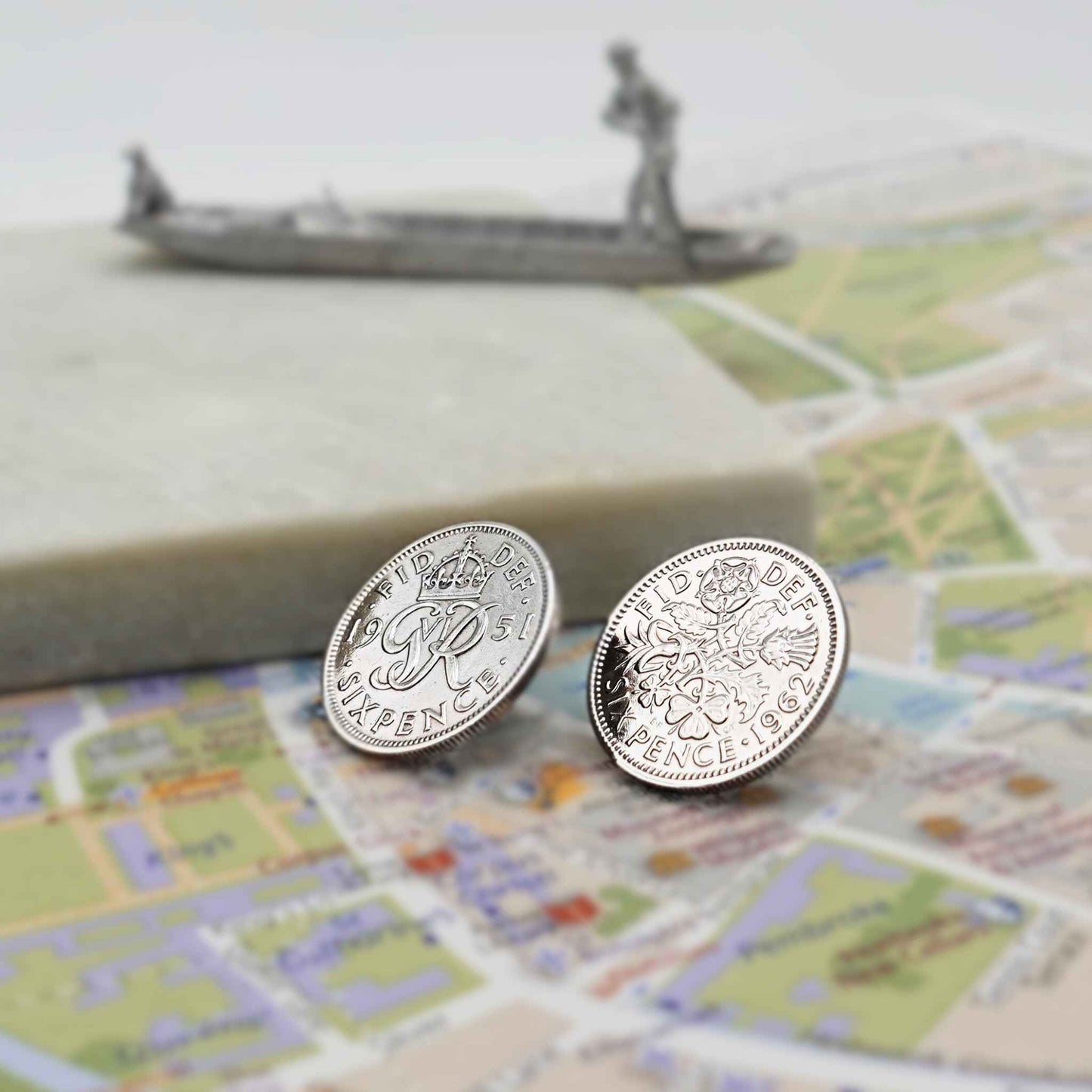Two british sixpence coin lapel pins showing Queen Elizabeth 2nd and King George 6th minting designs on a Cambridge map with punt in the background