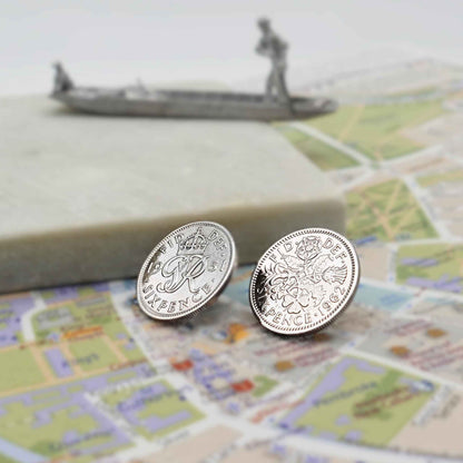 Two british sixpence coin lapel pins showing Queen Elizabeth 2nd and King George 6th minting designs on a Cambridge map with punt in the background