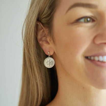 Close-up of a woman wearing silver American Dime coin earrings with a plain background