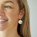 Close-up of a woman wearing an Irish threepence coin earring with a plain background.