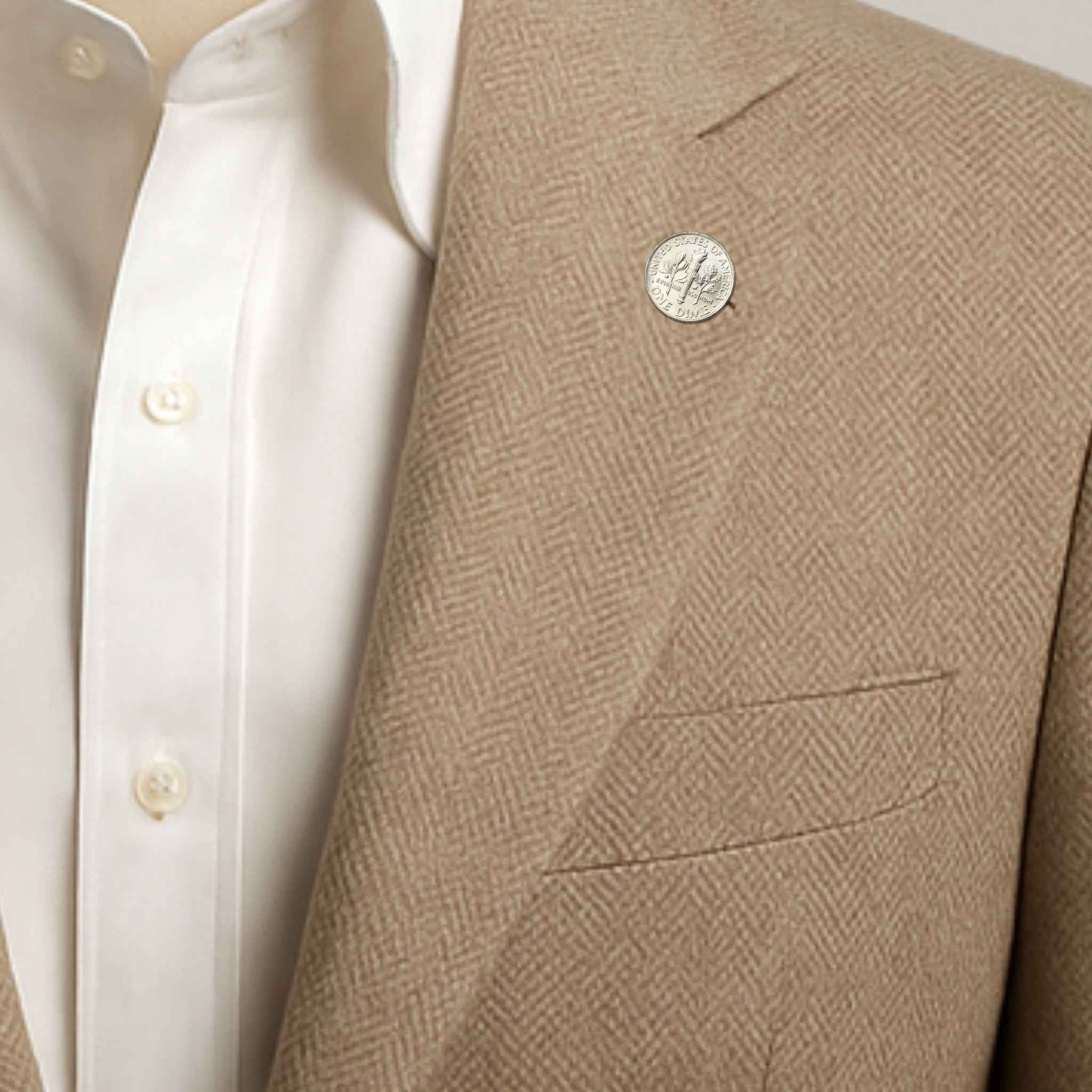 Close-up of a beige blazer with a US Dime coin lapel pin and white shirt underneath