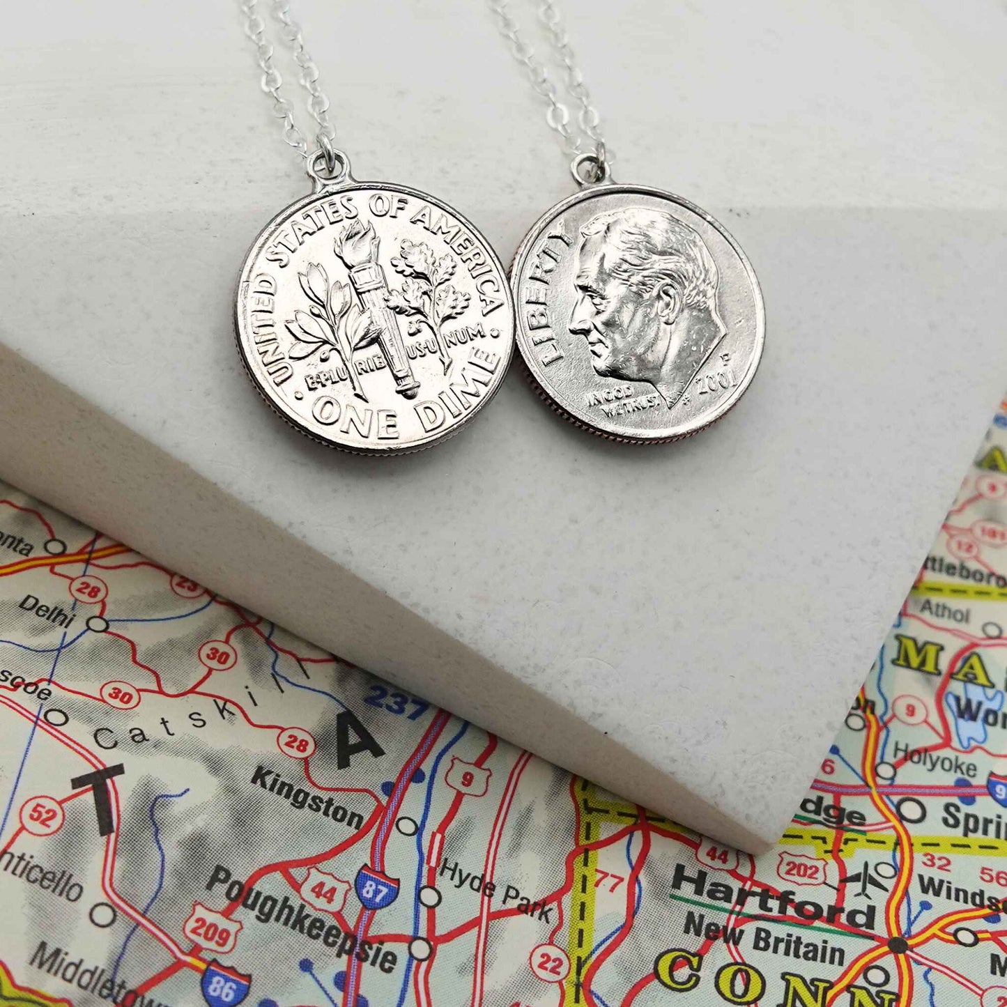 Two silver US Dime coin necklaces on a map background