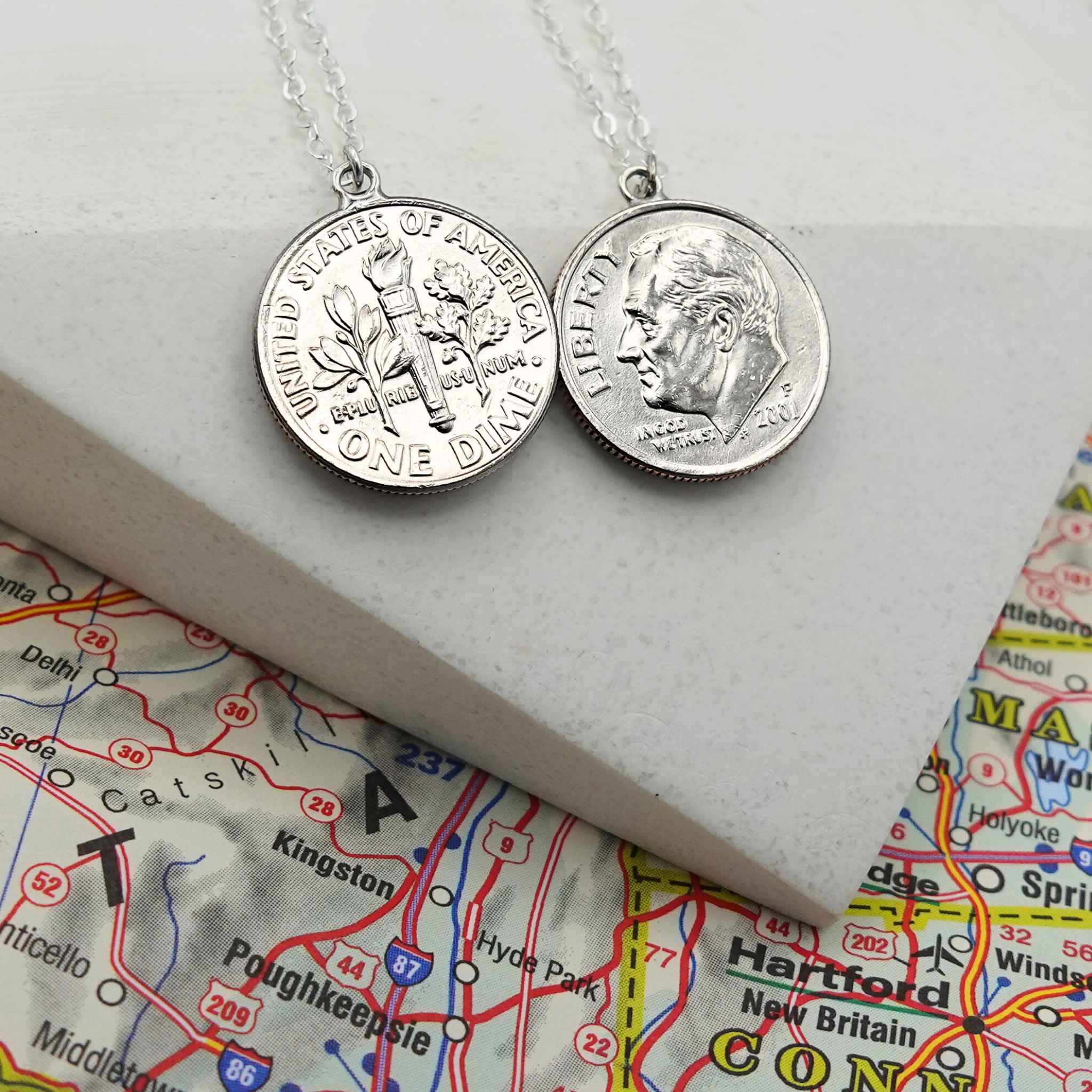 Two silver US Dime coin necklaces on a map background