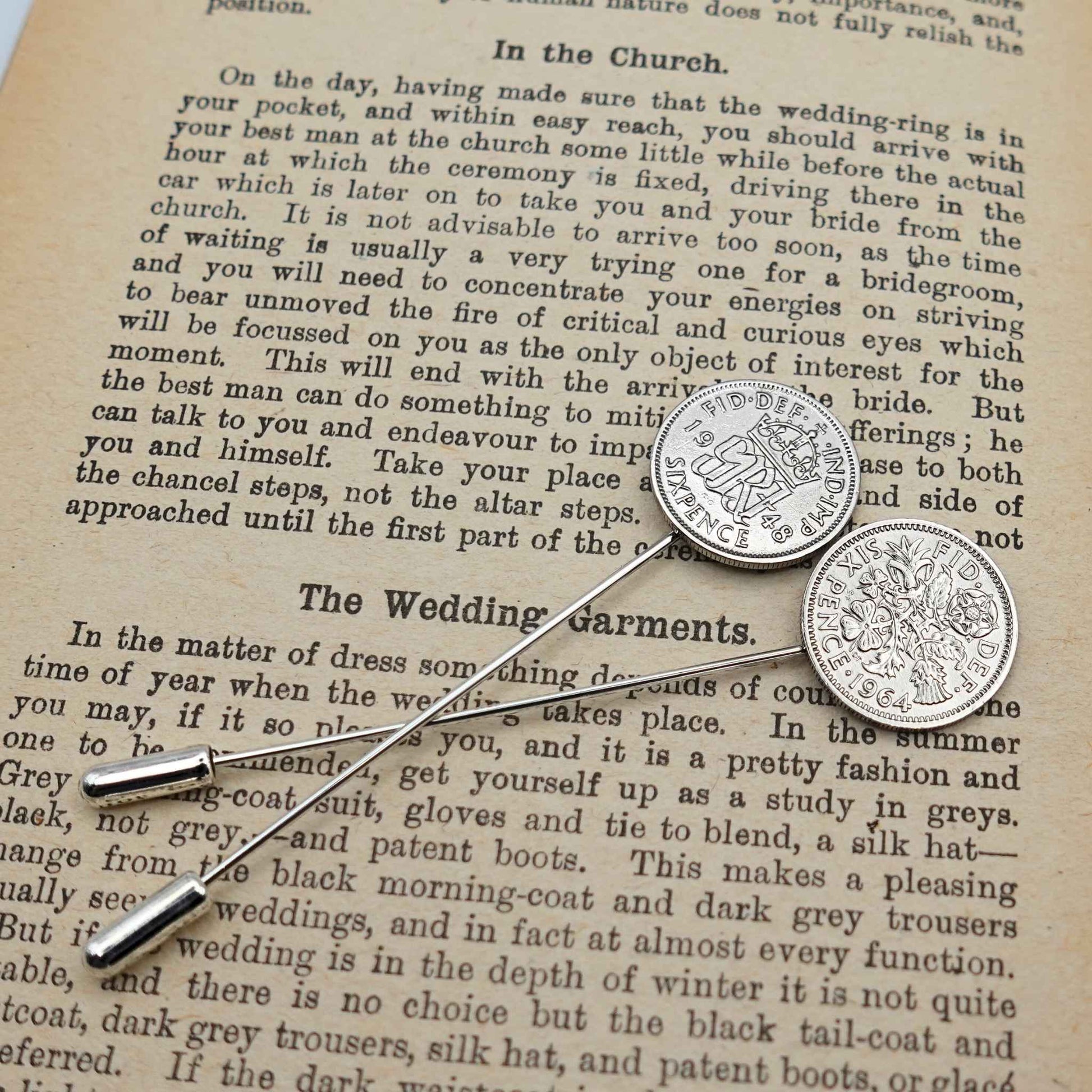 Silver sixpence coin tie pins on a text background