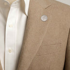 Close-up of a beige blazer with a textured pattern and a Queen Elizabeth 2nd sixpence coin lapel pin button, worn over a white shirt.
