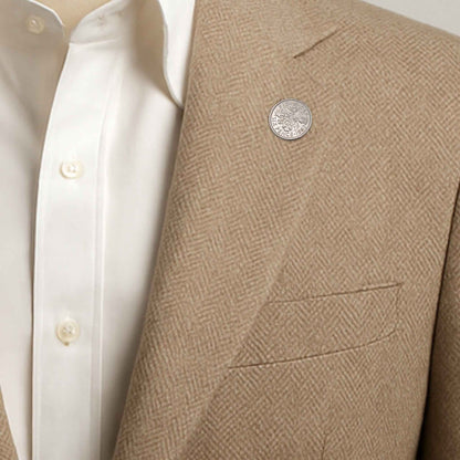 Close-up of a beige blazer with a textured pattern and a Queen Elizabeth 2nd sixpence coin lapel pin button, worn over a white shirt.