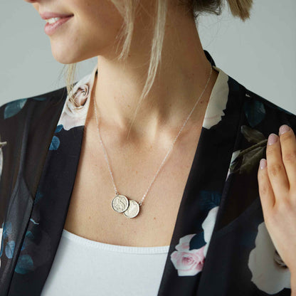 Woman wearing a delicate Irish threepence two coin pendant necklace with floral jacket