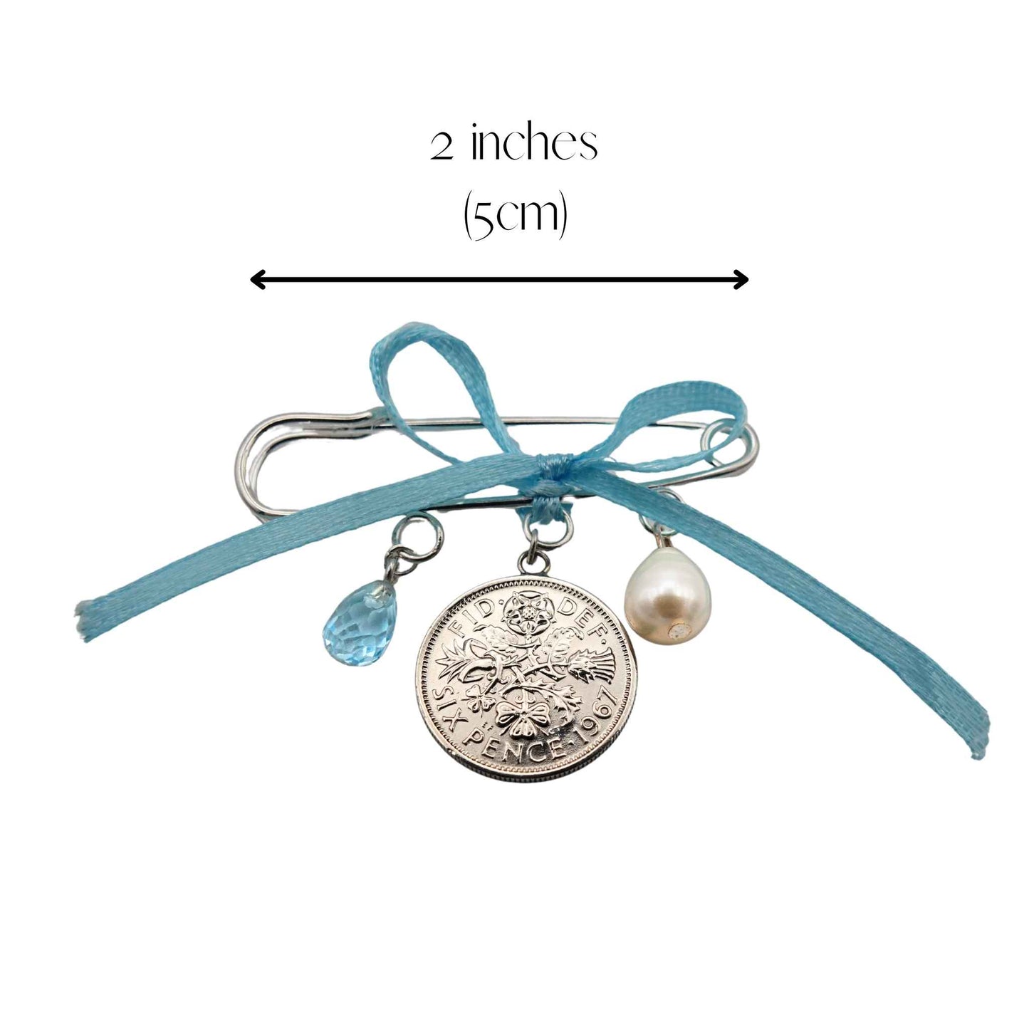 Bridal pin with sixpence coin, pearl, and blue topaz charms and a measurement label on a white background 