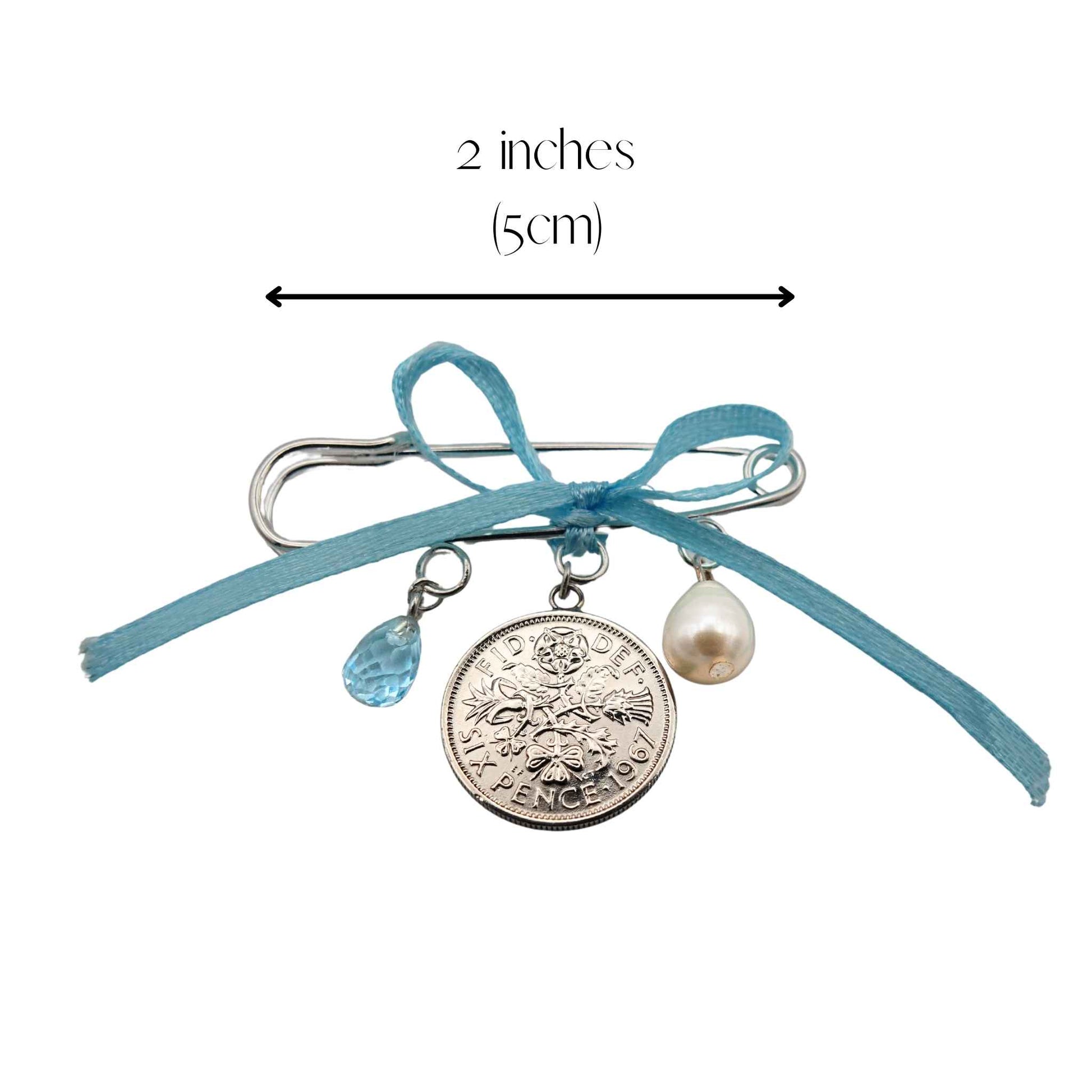 Bridal pin with sixpence coin, pearl, and blue topaz charms and a measurement label on a white background 