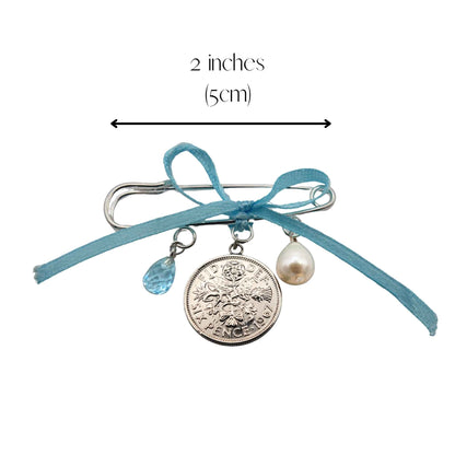 Bridal pin with sixpence coin, pearl, and blue topaz charms and a measurement label on a white background 