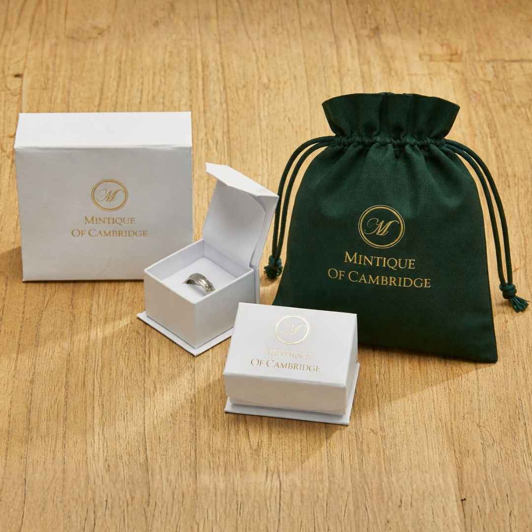 Jewelry set with ring, box, and green drawstring bag on a wooden surface, featuring Mintique of Cambridge branding.