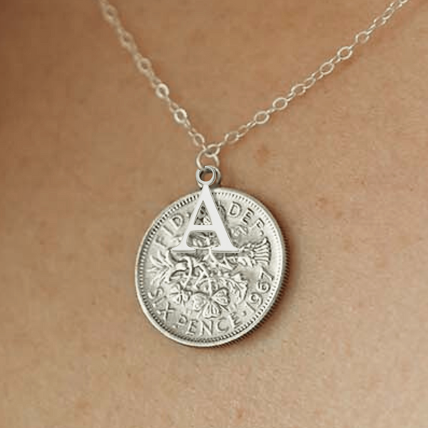 Silver sixpence coin necklace with an initial pendant on a person's neck