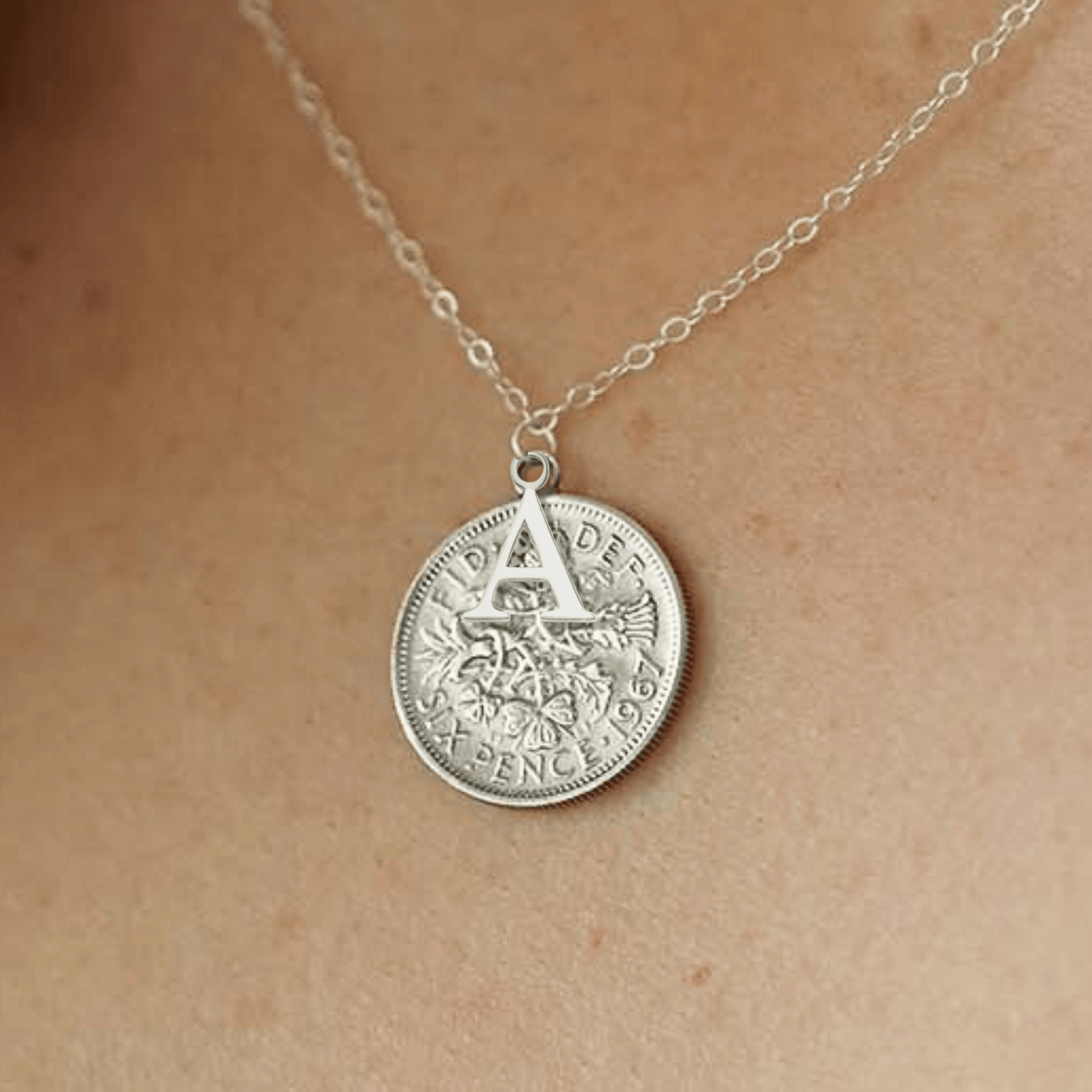 Silver sixpence coin necklace with an initial pendant on a person's neck