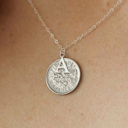 Silver sixpence coin necklace with an initial pendant on a person's neck
