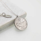 Silver sixpence coin necklace on a light gray surface