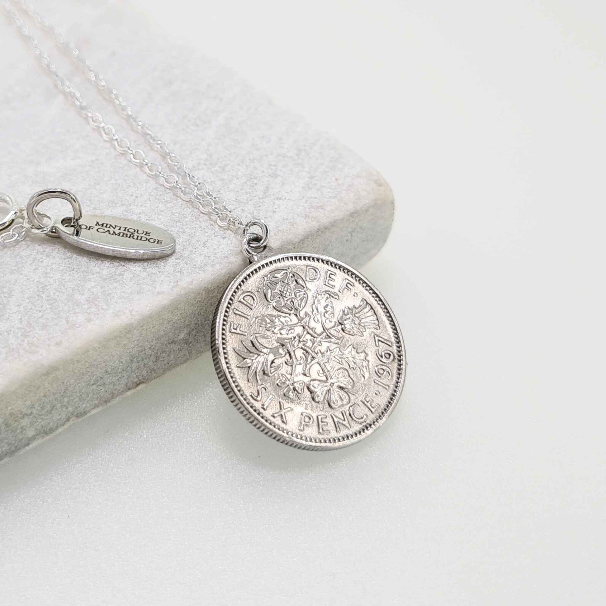 Silver sixpence coin necklace on a light gray surface