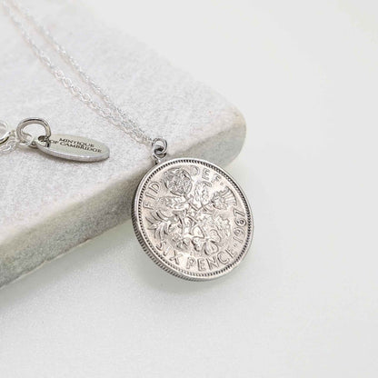 Silver sixpence coin necklace on a light gray surface