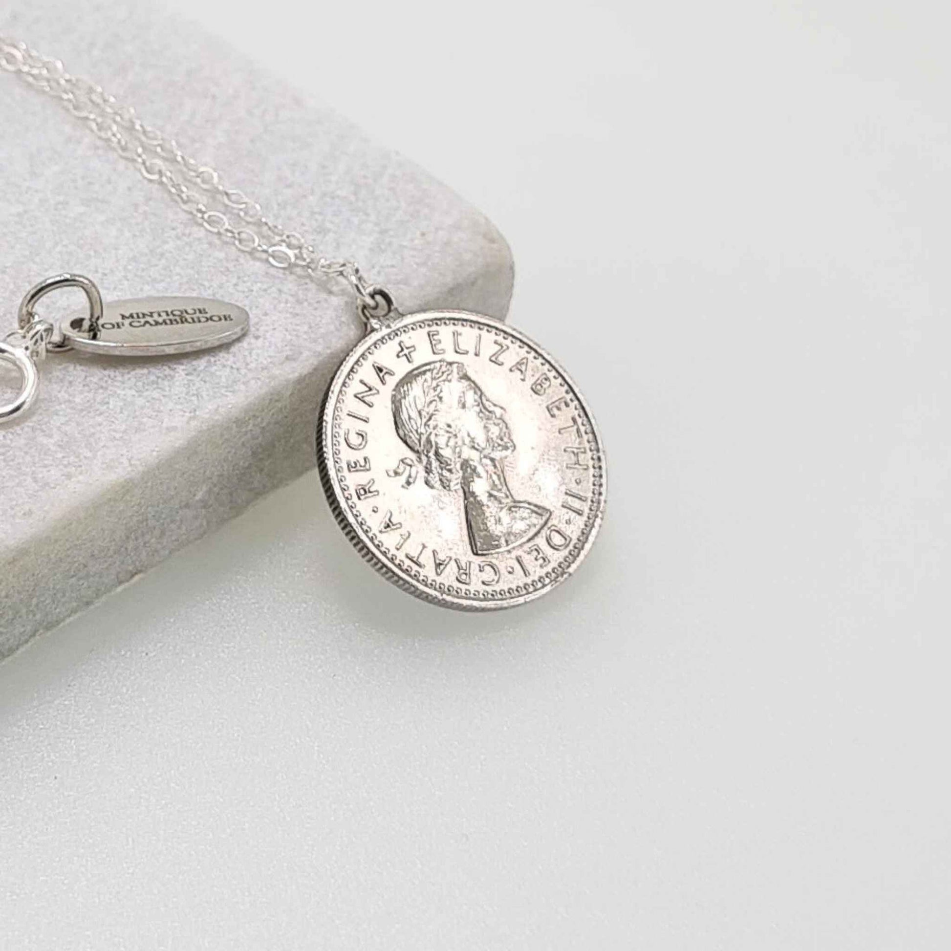 Silver British sixpence coin necklace on a light gray surface showing the head of Queen Elizabeth 2nd