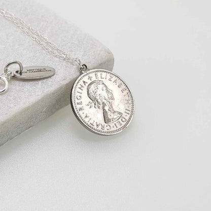 Silver British sixpence coin necklace on a light gray surface showing the head of Queen Elizabeth 2nd