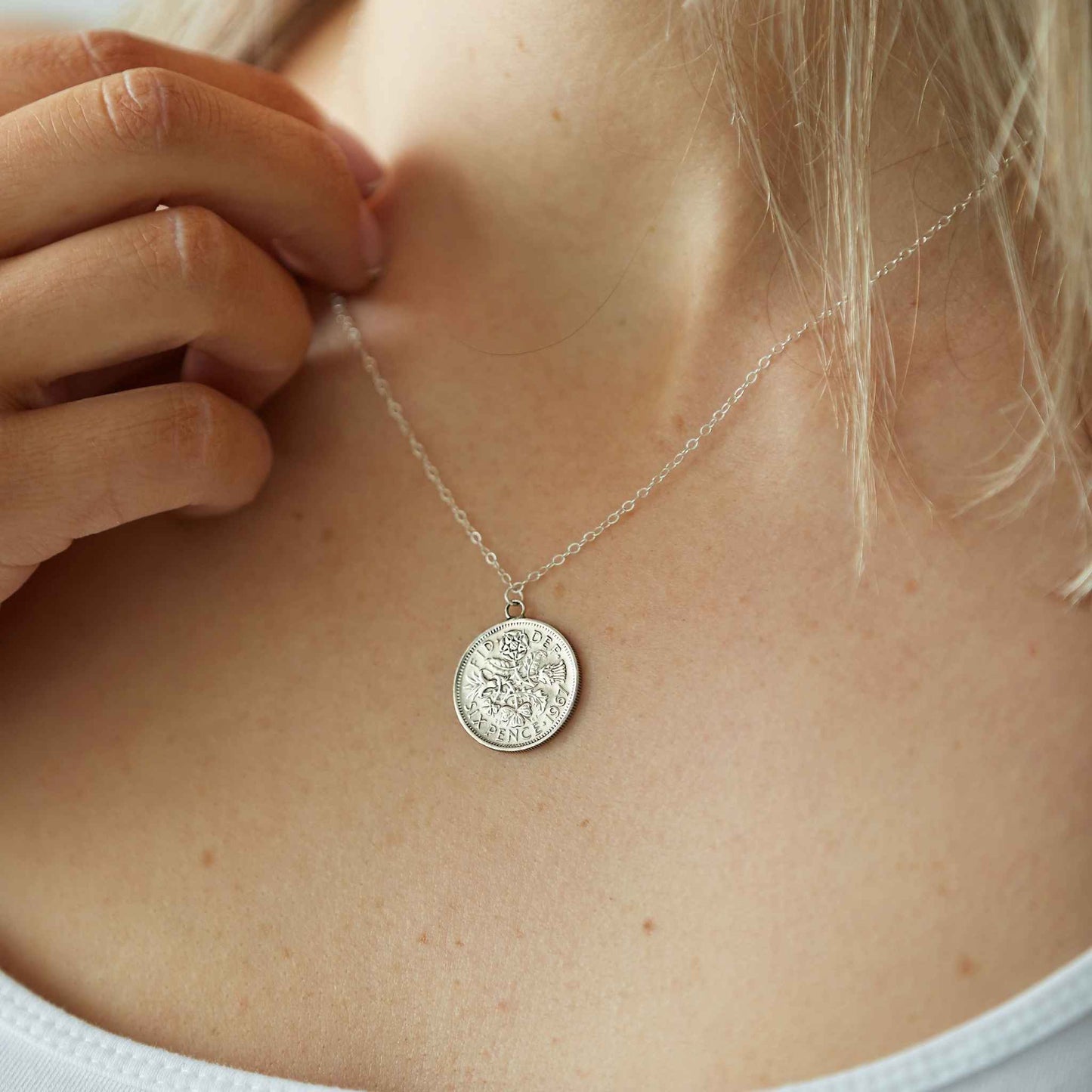 Close-up of a silver sixpence coin necklace pendant on a person's neck.