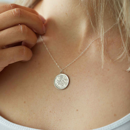 Close-up of a silver sixpence coin necklace pendant on a person's neck.