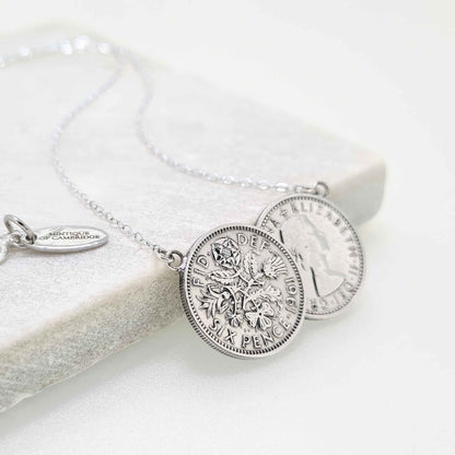 Silver two coin sixpence necklace on a tile with white background