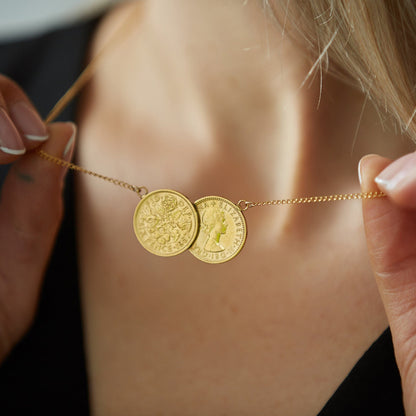 A close-up of a person wearing a necklace featuring two gold-plated sixpence coins on a chain, with one side of the coin showing a floral design and the other side Queen Elizabeth II.
