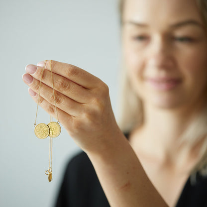 Woman holding a gold necklace with two sixpence coins against a neutral background